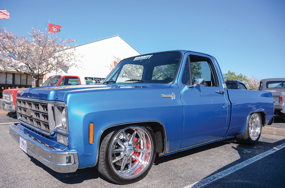 Landscape outdoor close-up photograph angle view of a vintage light blue Chevrolet Silverado C10 truck vehicle parked in a parking lot area nearby other random assorted cars during the day