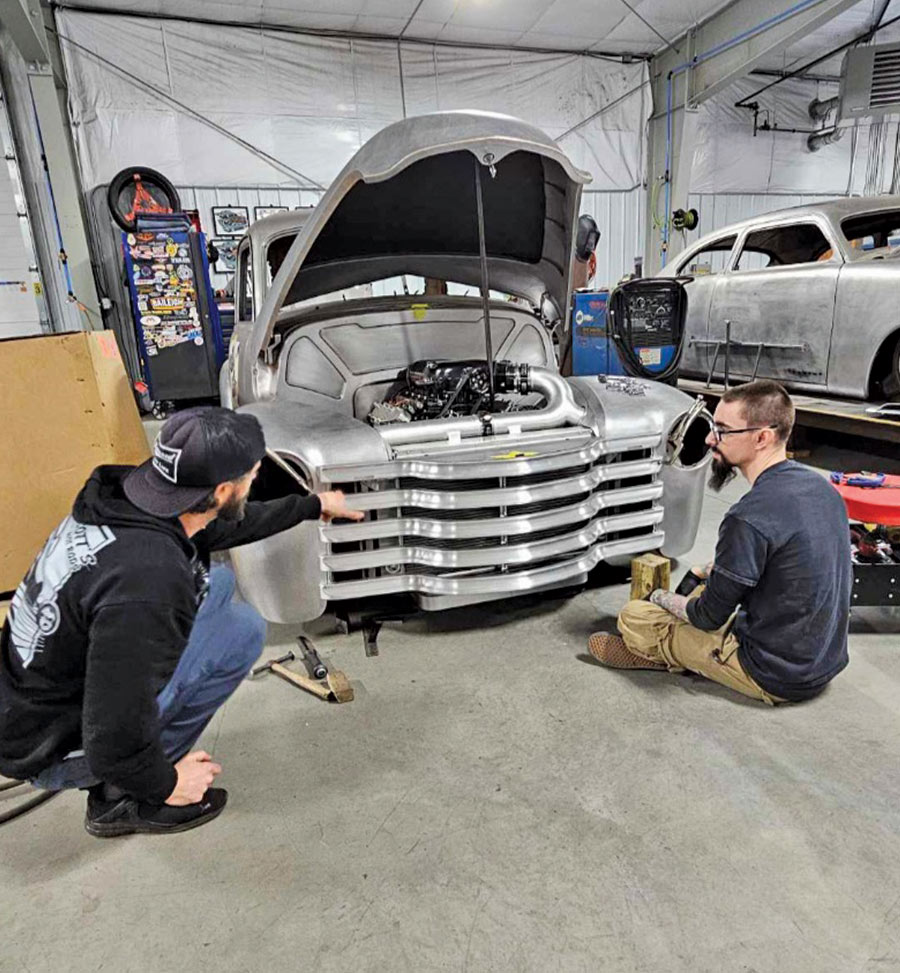 two men sitting on the floor in front of a '51 Chevy