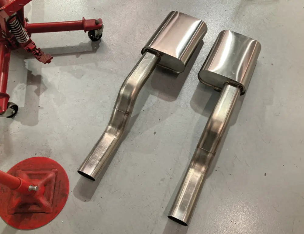 both mufflers and their respective S-bend placed side by side on a auto shop floor