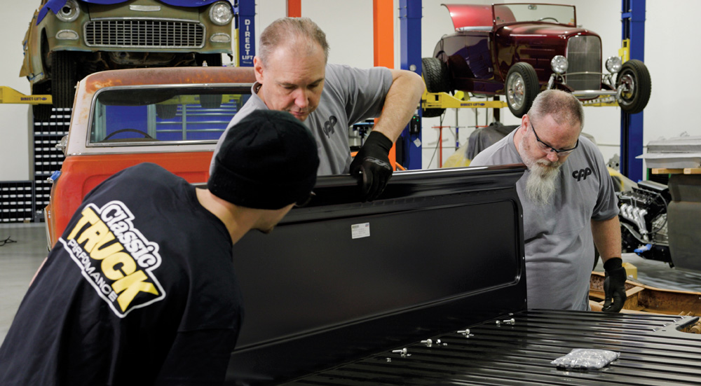 Team installing a new black tailgate on a 1967-1972 GMC truck during the restoration process
