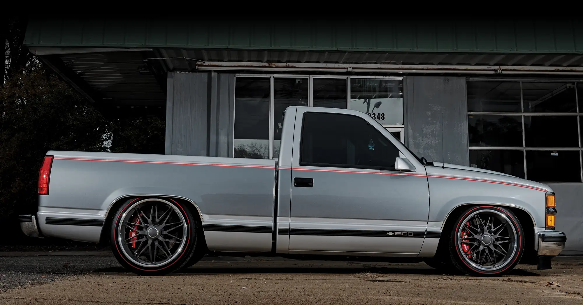 Side profile of a lowered silver 1994 Chevrolet C1500 with black wheels, red pinstripes, and chrome accents