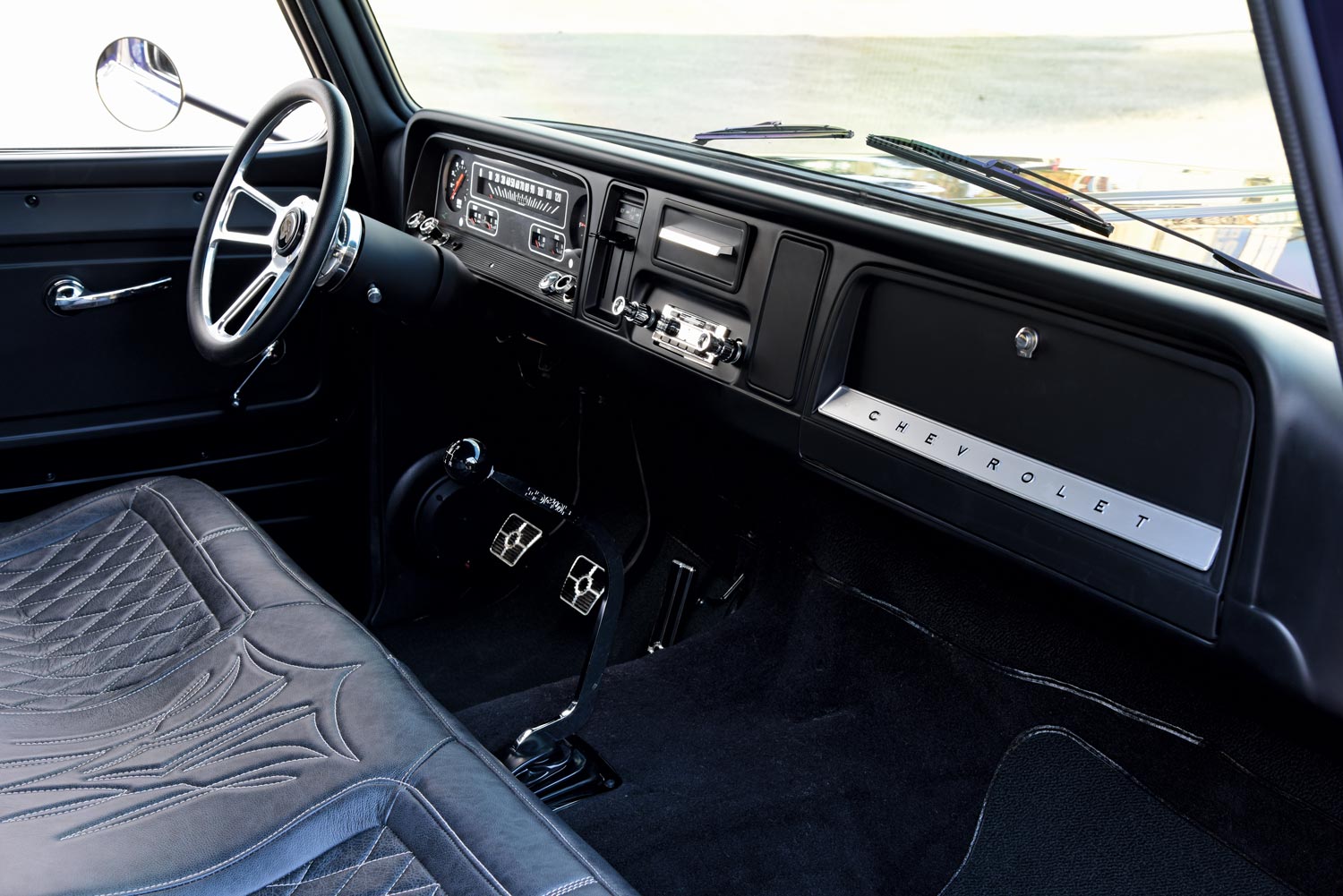 The dashboard of a 1966 Chevrolet C10 with a clean black interior, custom steering wheel, and retro-modern gauges