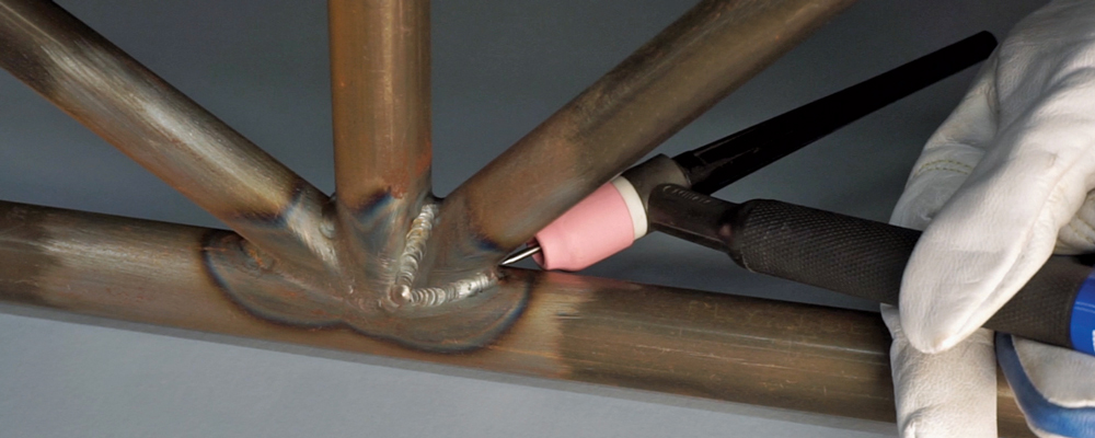 Operator using a TIG torch with a pink ceramic nozzle for welding metal tubing