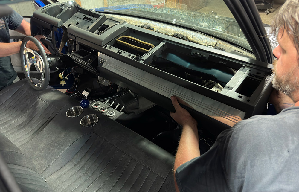 Two people carefully removing the dashboard from a 1990s Chevrolet CK 1500