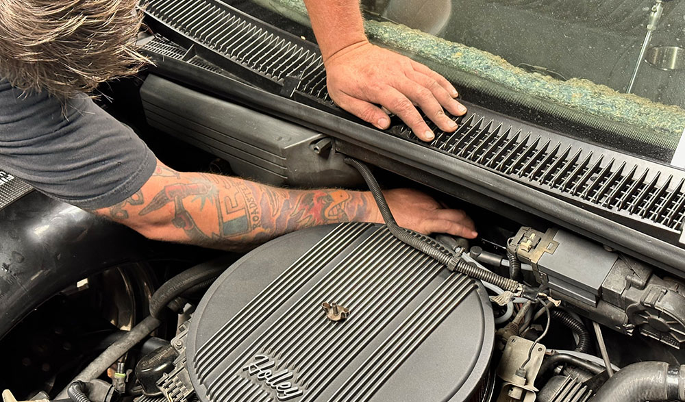 Working under the hood near the windshield of a 1990s Chevrolet CK 1500 to install air conditioning components
