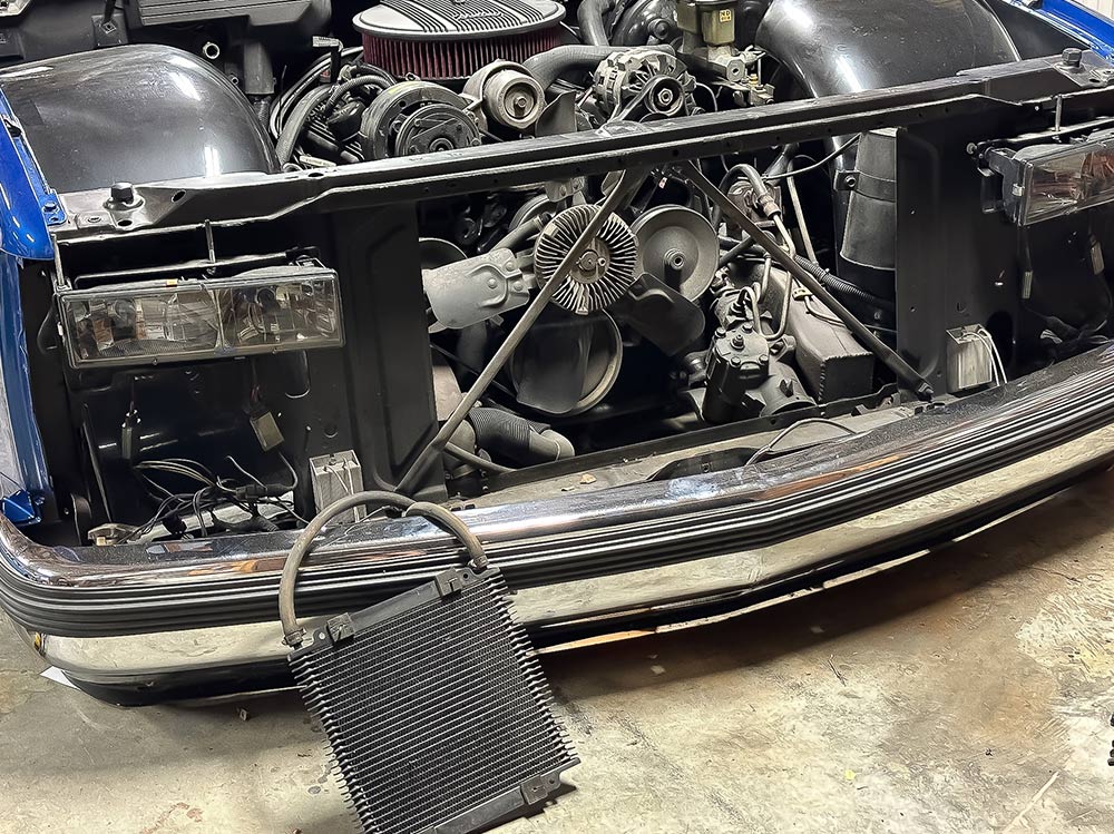 Front grille removed, exposing the engine bay of a blue 1990s Chevrolet CK 1500 during installation