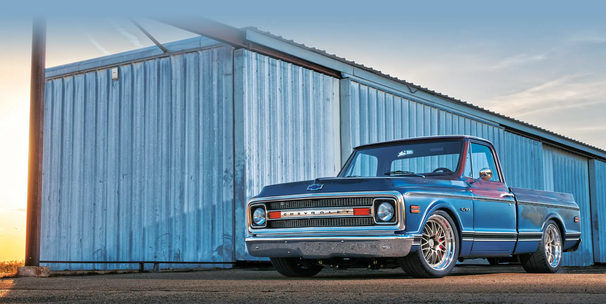 Low angle side profile of 1969 Chevy C10 truck, rustic warehouse, sunset sky