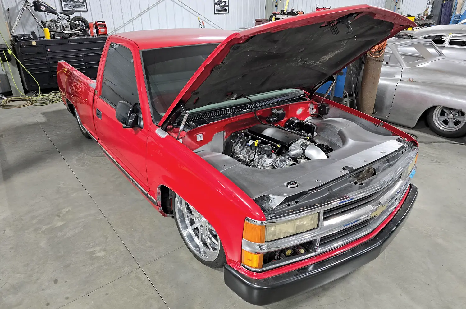 Red OBS with open hood showcasing engine modifications in a garage