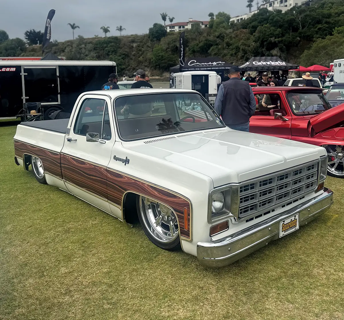 White square-body Chevy truck with wood panel accents and lowered stance at a truck show