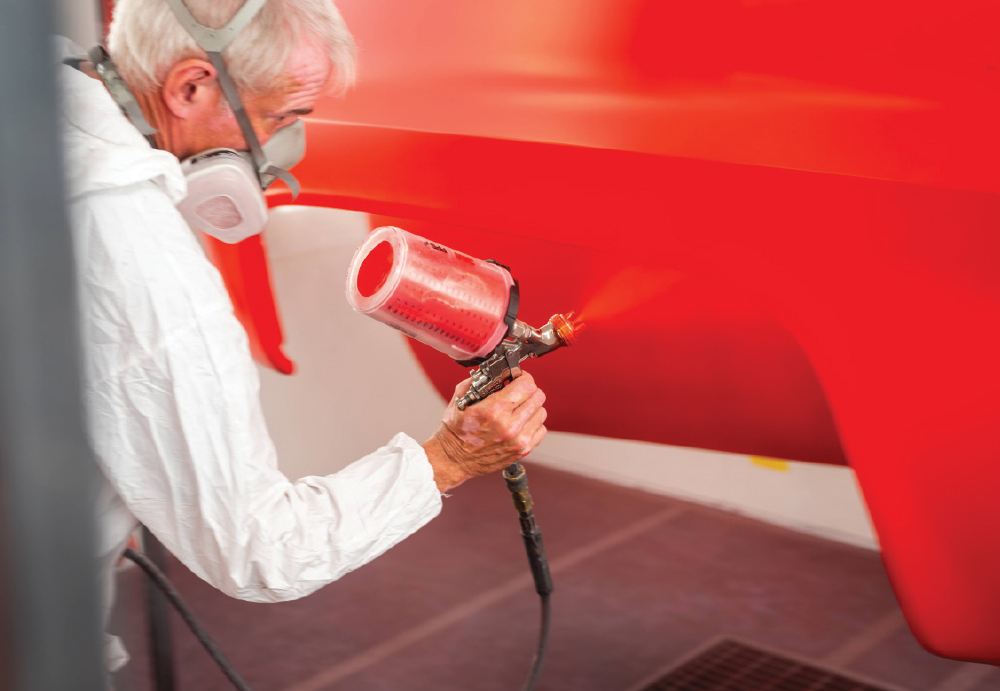 Painter applying fresh red coat to the GMC K2500 body, achieving a smooth and vibrant finish