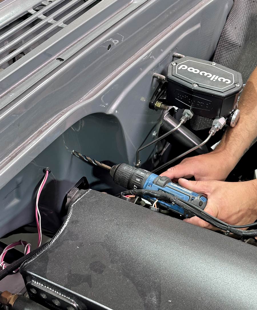 Drilling the firewall to prepare for Lokar throttle cable installation in a Chevy C10