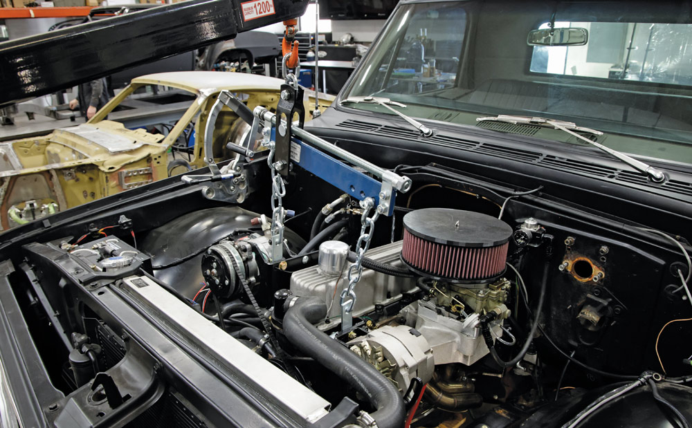 Engine crane lifting small-block engine into the Chevy C10's engine bay during custom build