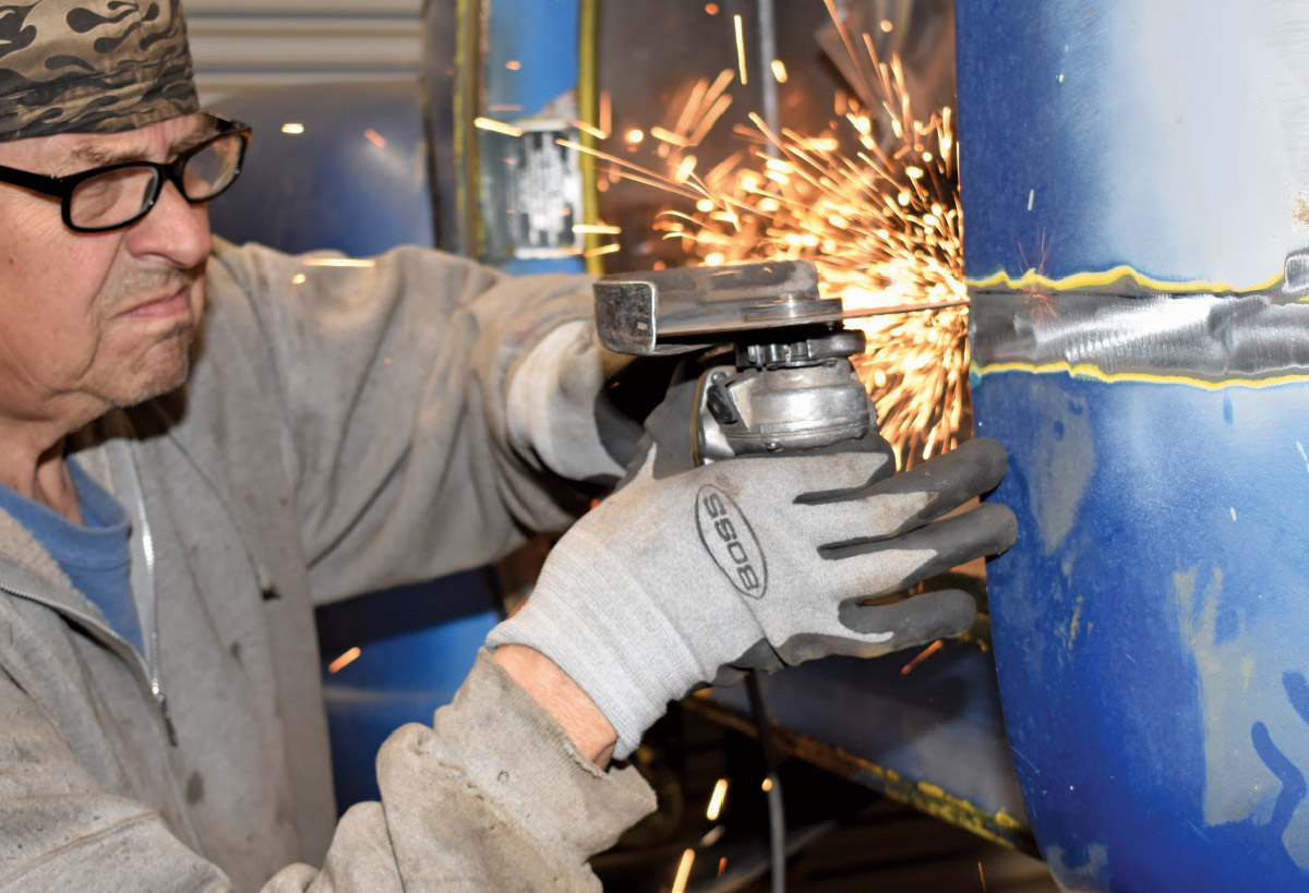 A fabricator using an angle grinder to smooth the welded seam on a truck cab corner