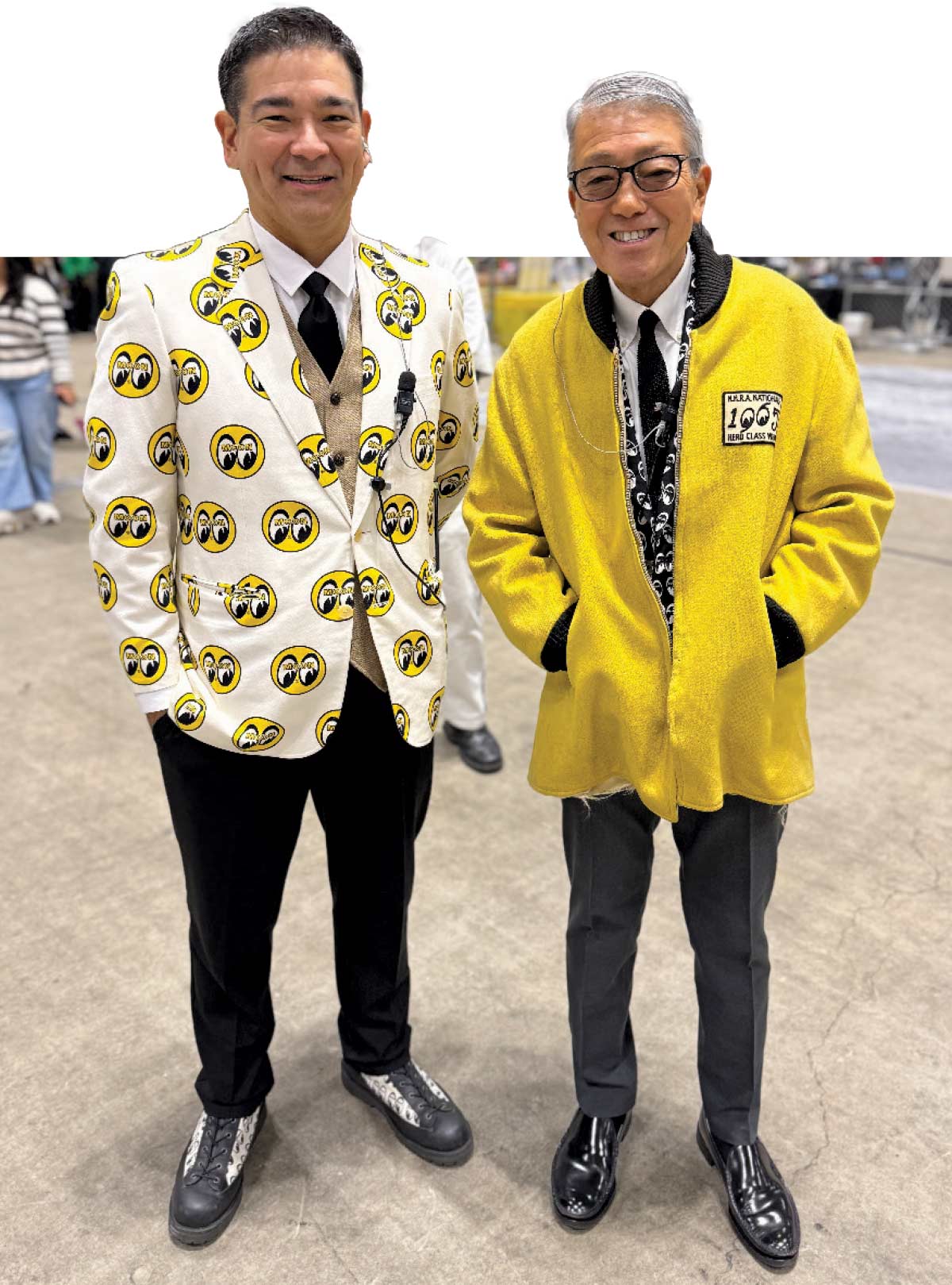 Two men in Mooneyes attire – One in a smiley-face blazer, the other in a yellow Mooneyes jacket
