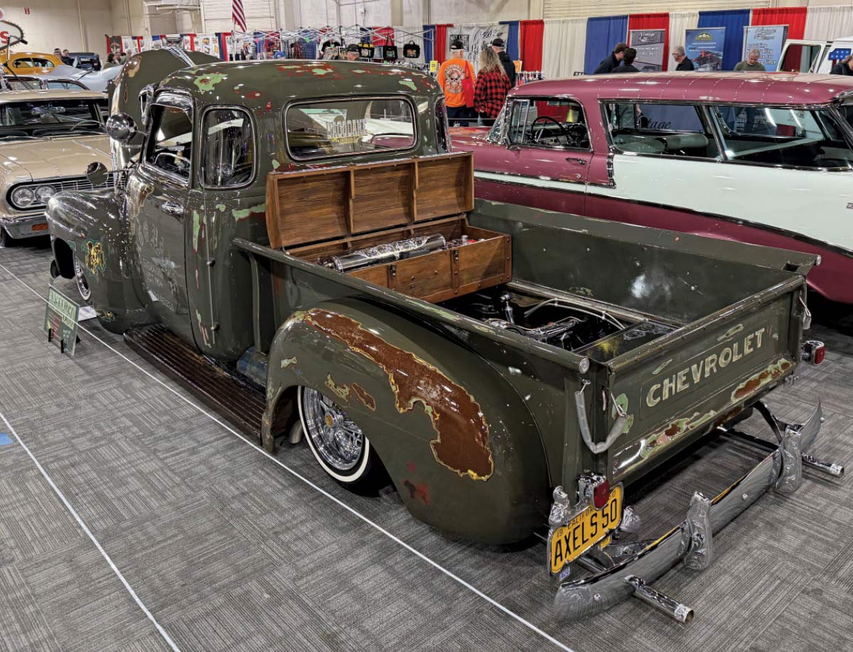 3/4 rear view of dark green truck with hood popped open decorated with various decals