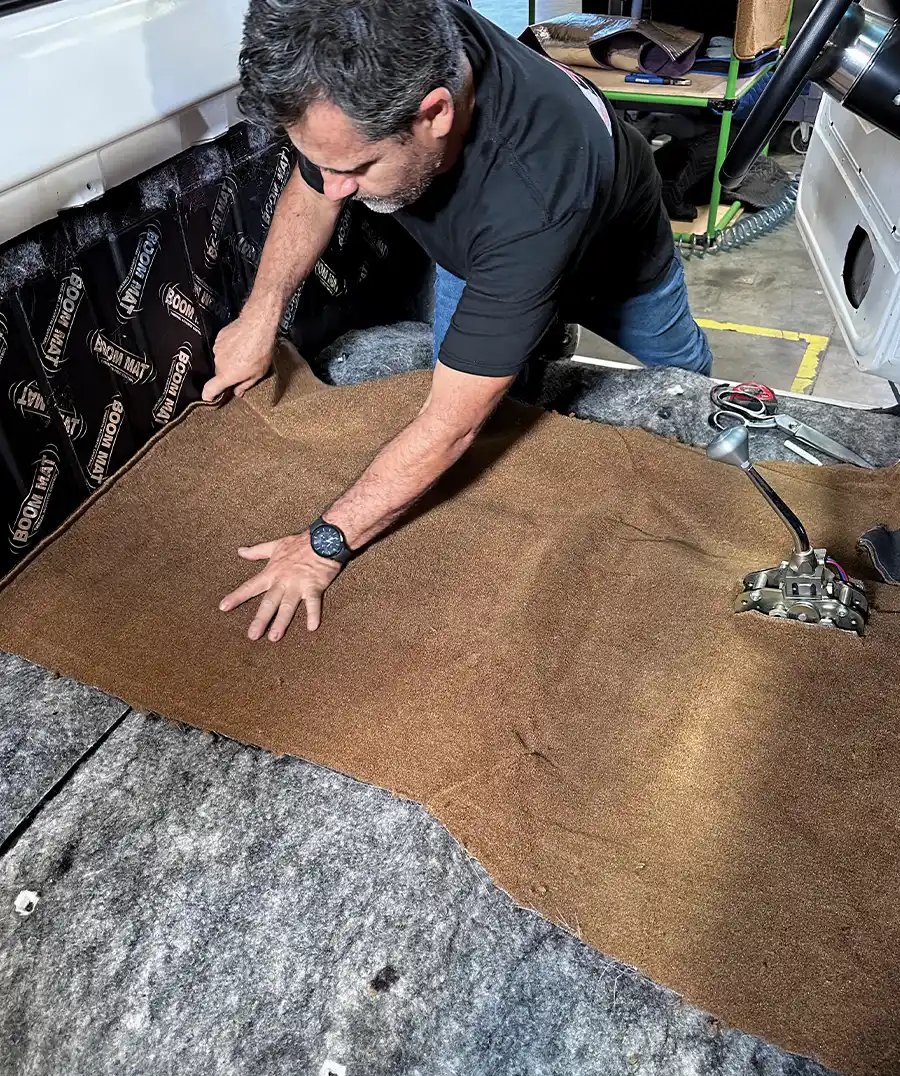 Professional installing brown carpet along C10’s rear cab wall
