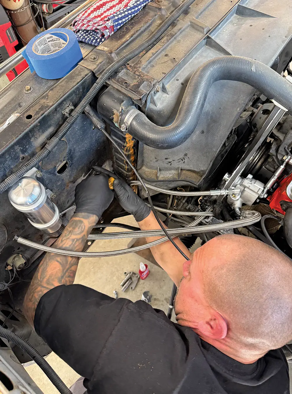 Tech routes braided steel lines through the engine bay firewall of a 1971 Chevy C10 for power steering setup