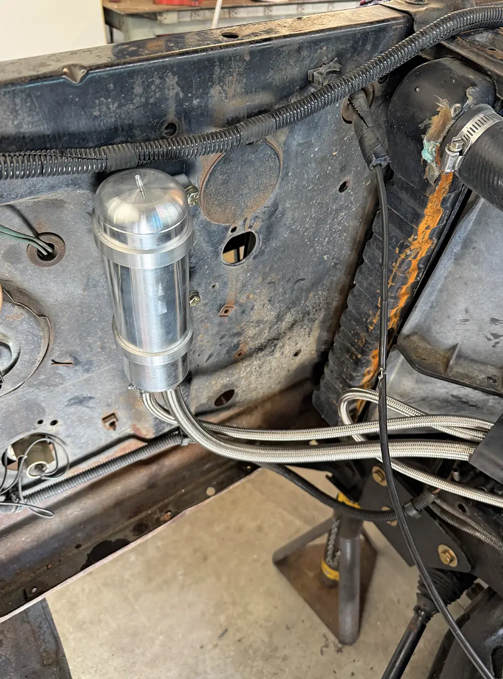 Polished aluminum remote reservoir mounted to firewall with braided hoses secured underneath