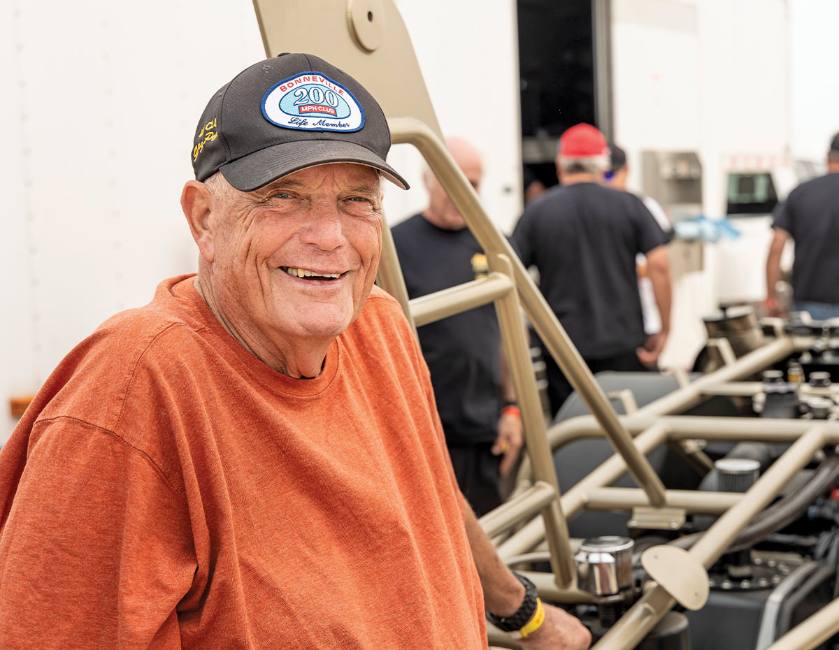 George Poteet wearing Bonneville 200 MPH Club hat beside land speed race car chassis at dry lakes event