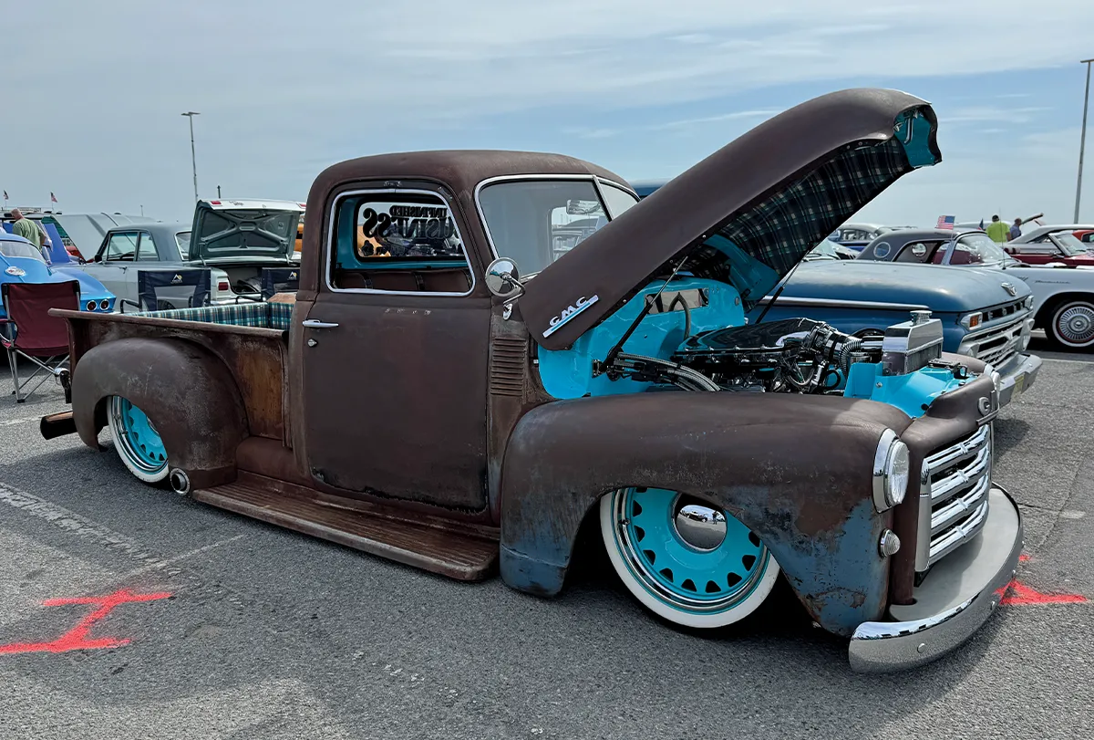 Custom classic pickup with a distressed paint job, wood-slat bed, and a checkered interior, representing a unique restomod build at an outdoor event.