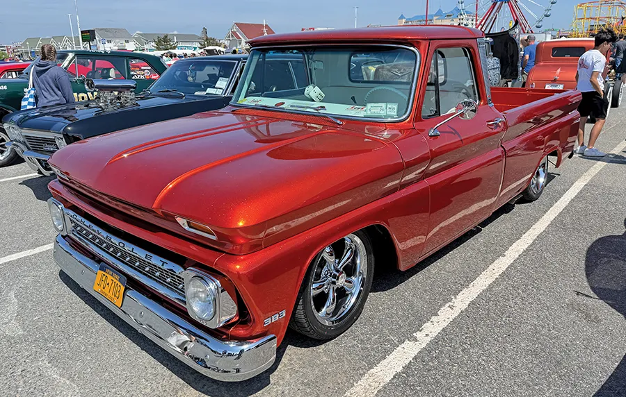 Restored shiny red classic Chevrolet pickup truck with chrome wheels and a lowered stance, on display at an outdoor car show.
