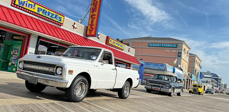 Restored Chevrolet truck with a white paint job and chrome accents, on display at a classic car show on a sunny boardwalk.