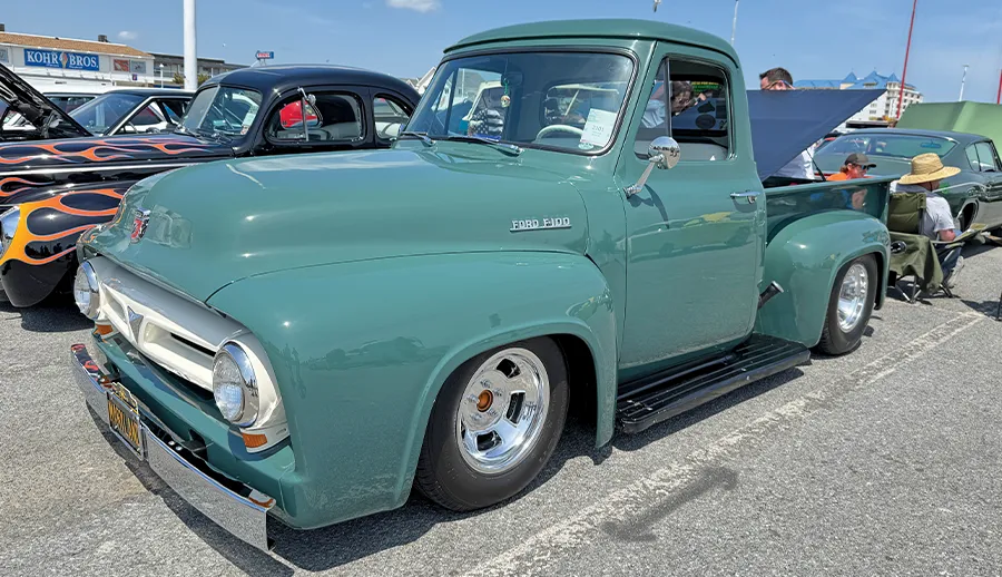 Vintage Ford truck with a two-tone teal and white paint job, chrome accents, and a modern stance, on display at a sunny event.