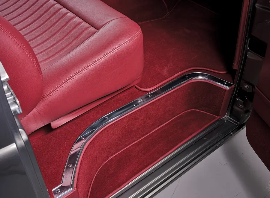 Detail shot of a restored vintage truck's cab, highlighting the matching red plush carpet, custom upholstery, and polished metal accents.
