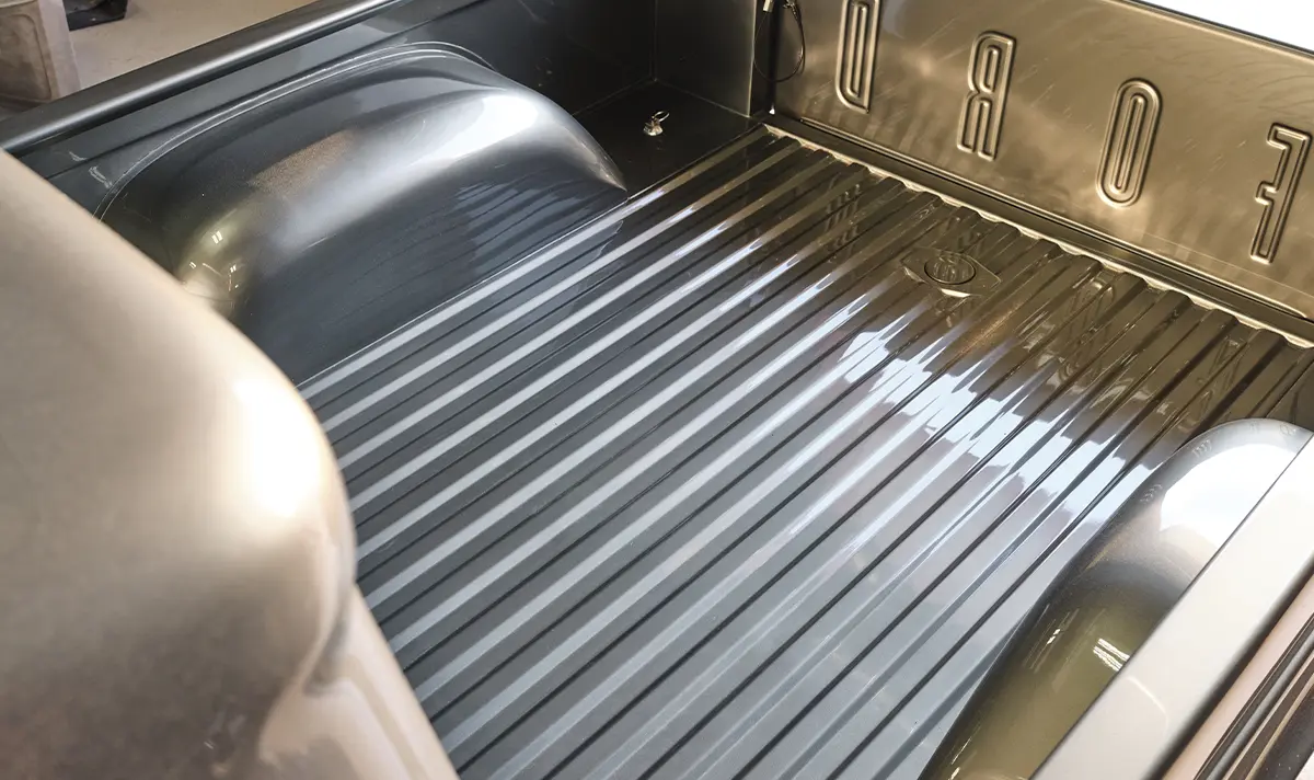 Truck bed of a restored classic Ford pickup, showing the clean gray-painted metal floor with a high-gloss finish and 'FORD' stamped into the tailgate.