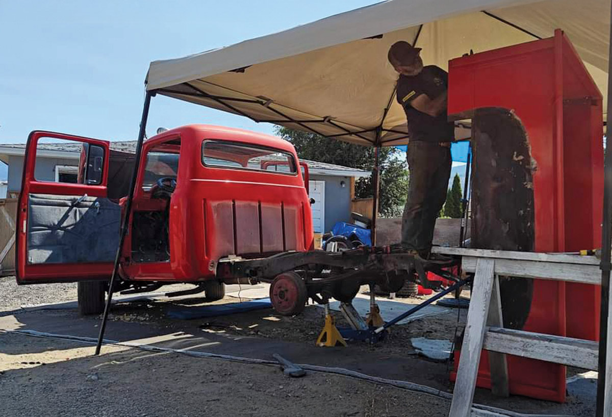 A red classic Ford pickup truck, partially disassembled and undergoing restoration. 