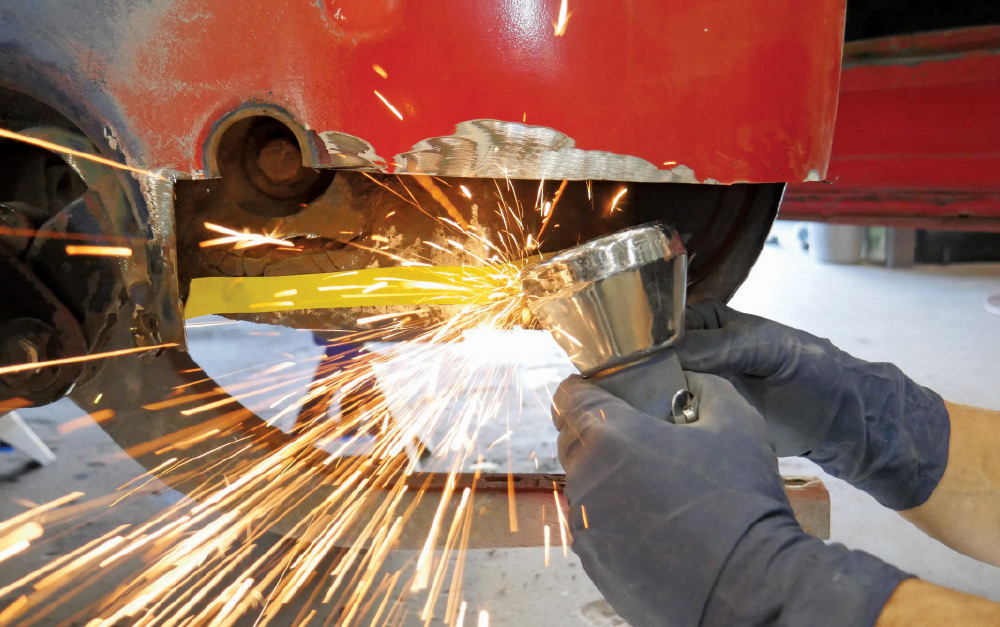 A close-up action shot of a person using a grinder to cut into the metal body of a red classic Ford pickup truck.