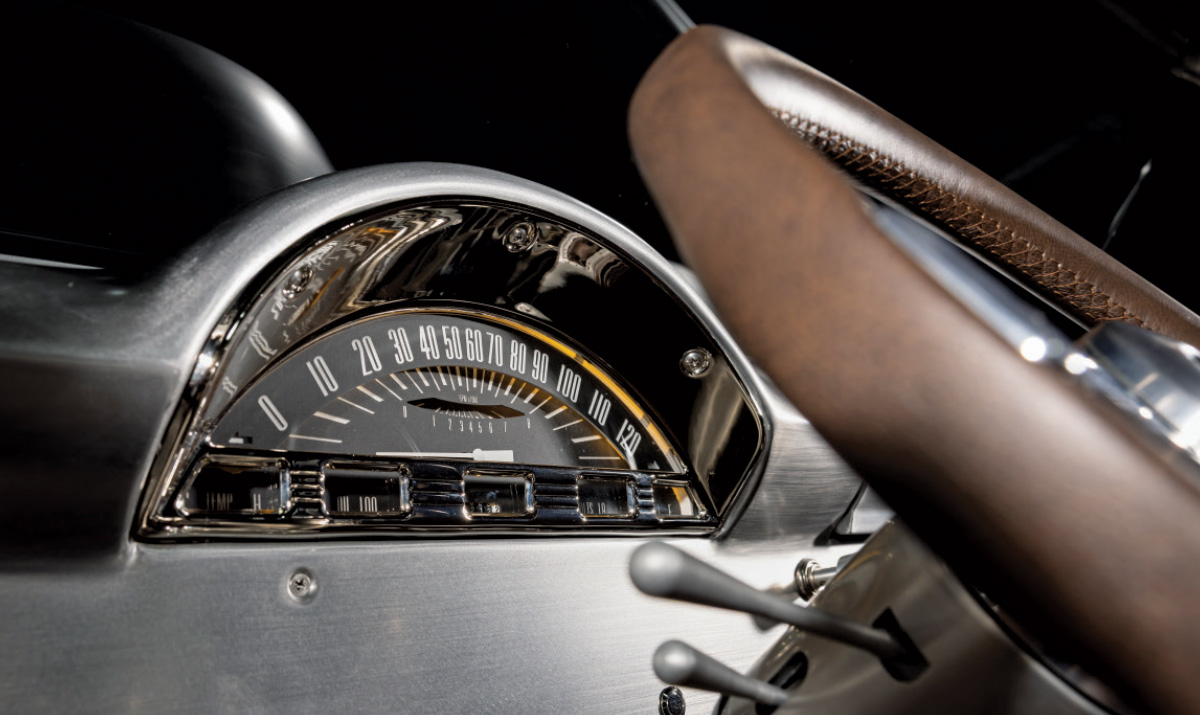 A close-up of the dashboard of a custom classic pickup truck. The image focuses on a highly detailed, vintage-style speedometer and gauge cluster with a chrome bezel. 