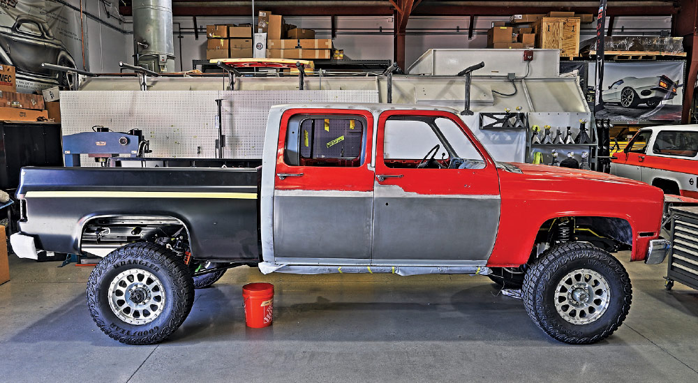 1985 chevy squarebody crew cab mid-build with raw panels, red cab and goodyear wrangler off-road tires