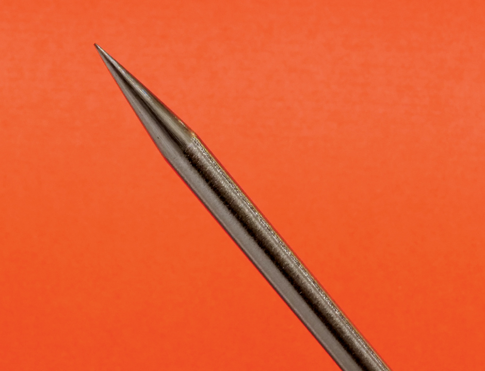 Single TIG tungsten electrode, long taper tip, close-up, orange background