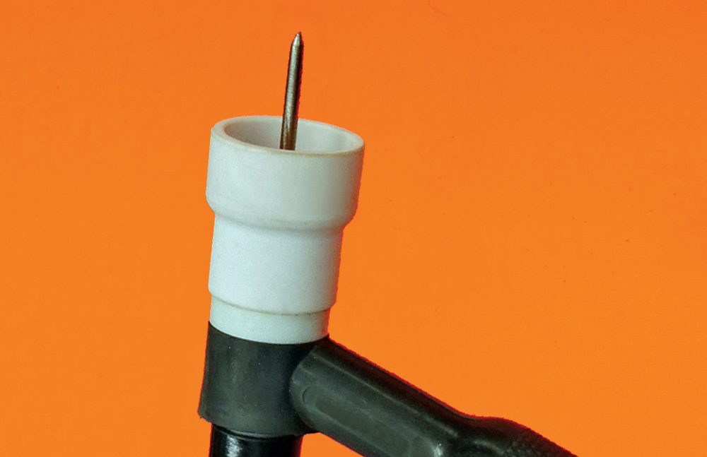 TIG torch, white ceramic cup, centered tungsten, partial handle in frame, orange background