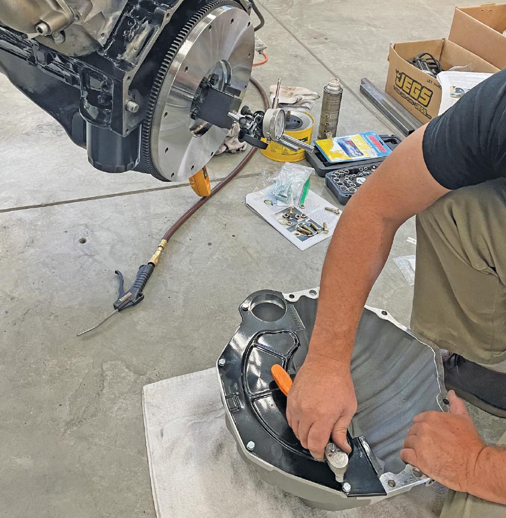 V8 engine block on hoist, mechanic installing bellhousing component, workshop assembly