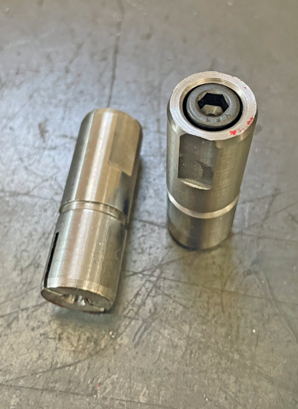 Two metallic bushings on workbench, solid cylinder and sleeve bearing components