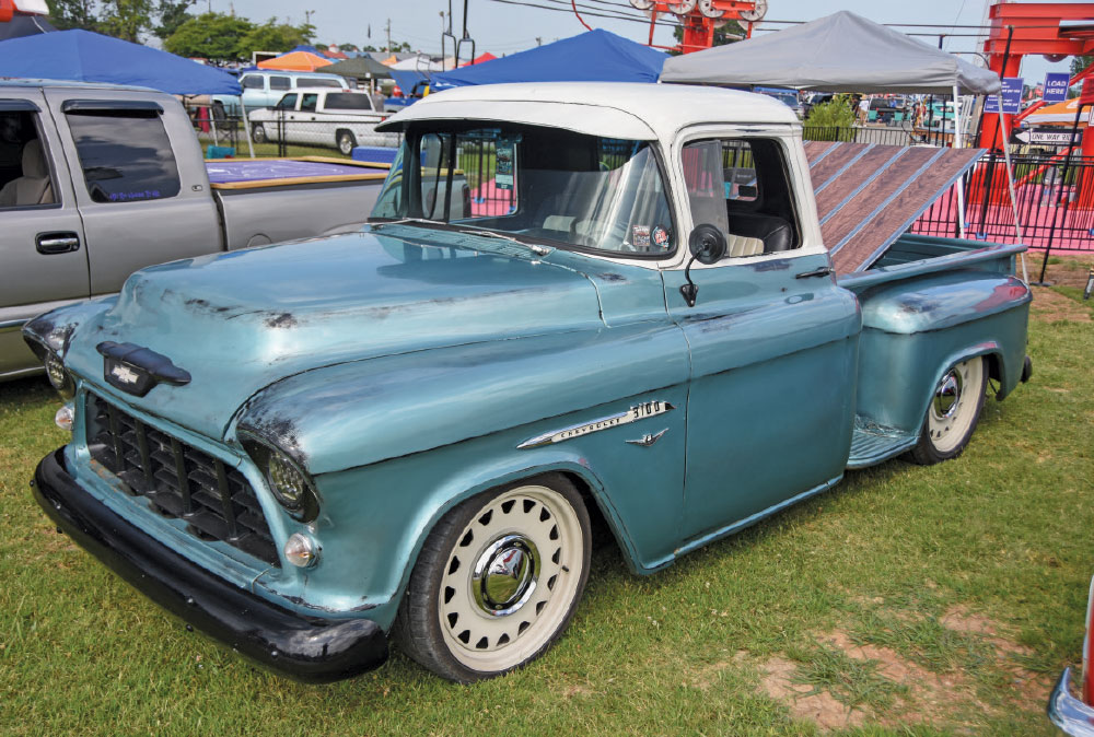 A vintage, low-slung blue and white Chevrolet 3100 pickup truck with a wood bed cover and white steel wheels, parked on the grass.