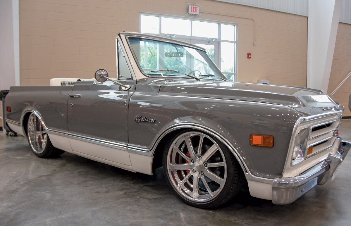 A restored, lowered gray and white Chevrolet K5 Blazer convertible with custom chrome wheels and red brake calipers, displayed indoors.