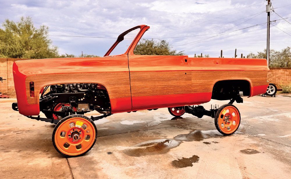 Exterior side view of an orange Chevrolet C10 body shell with wood-grain sides, engine exposed, on a chassis with orange wheels.