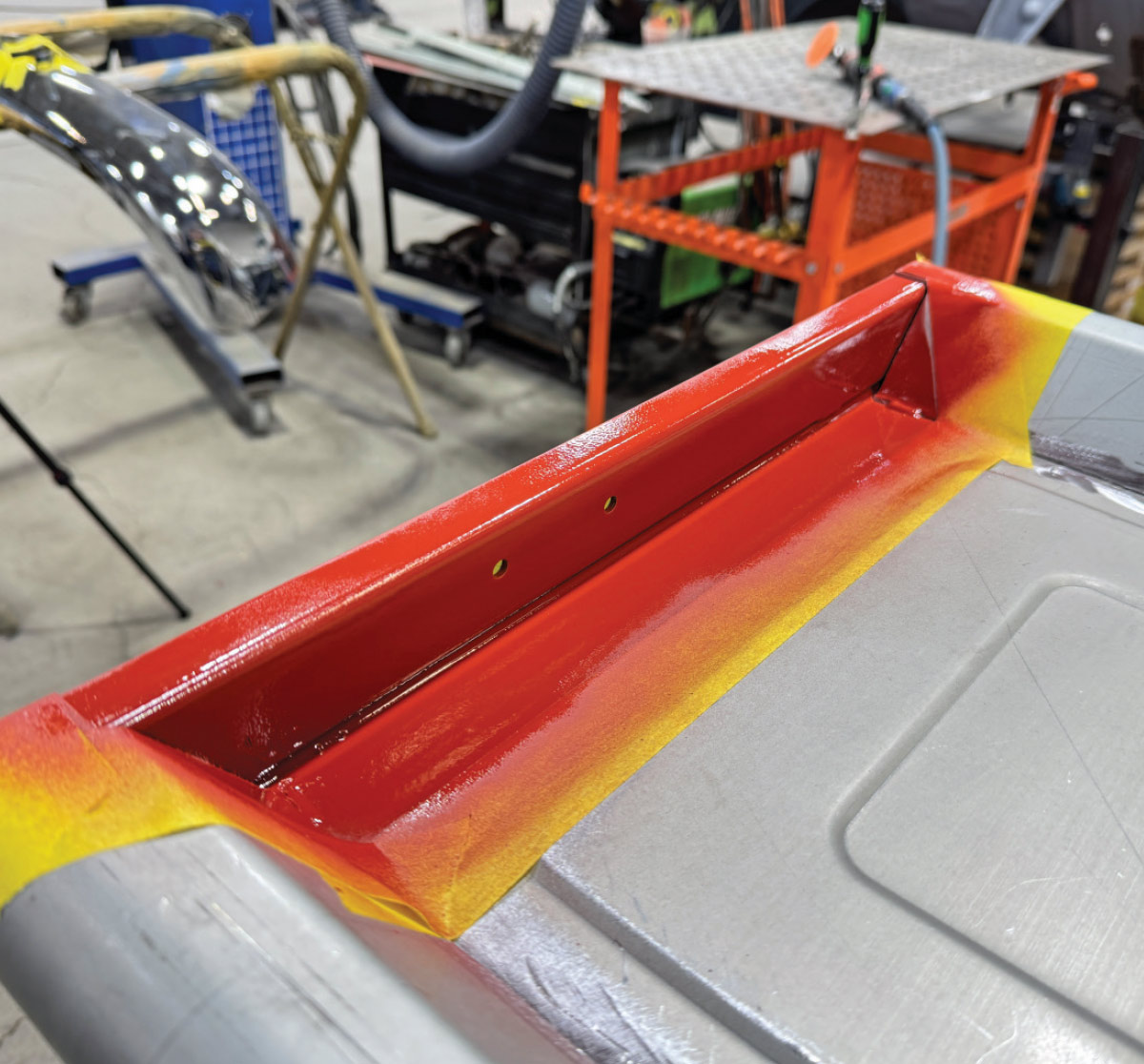 Red-painted reinforcement panel, yellow masking tape, triangular gussets, chrome bumper nearby