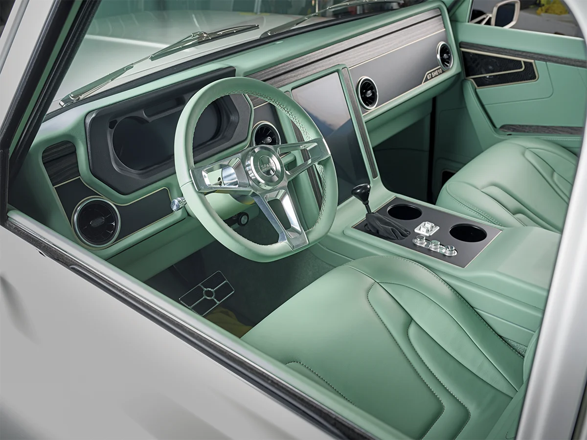 Customized interior of a vintage GMC/Chevrolet truck featuring light green leather seats, a matching steering wheel, and a modern, vertically-oriented digital display in the center dashboard.