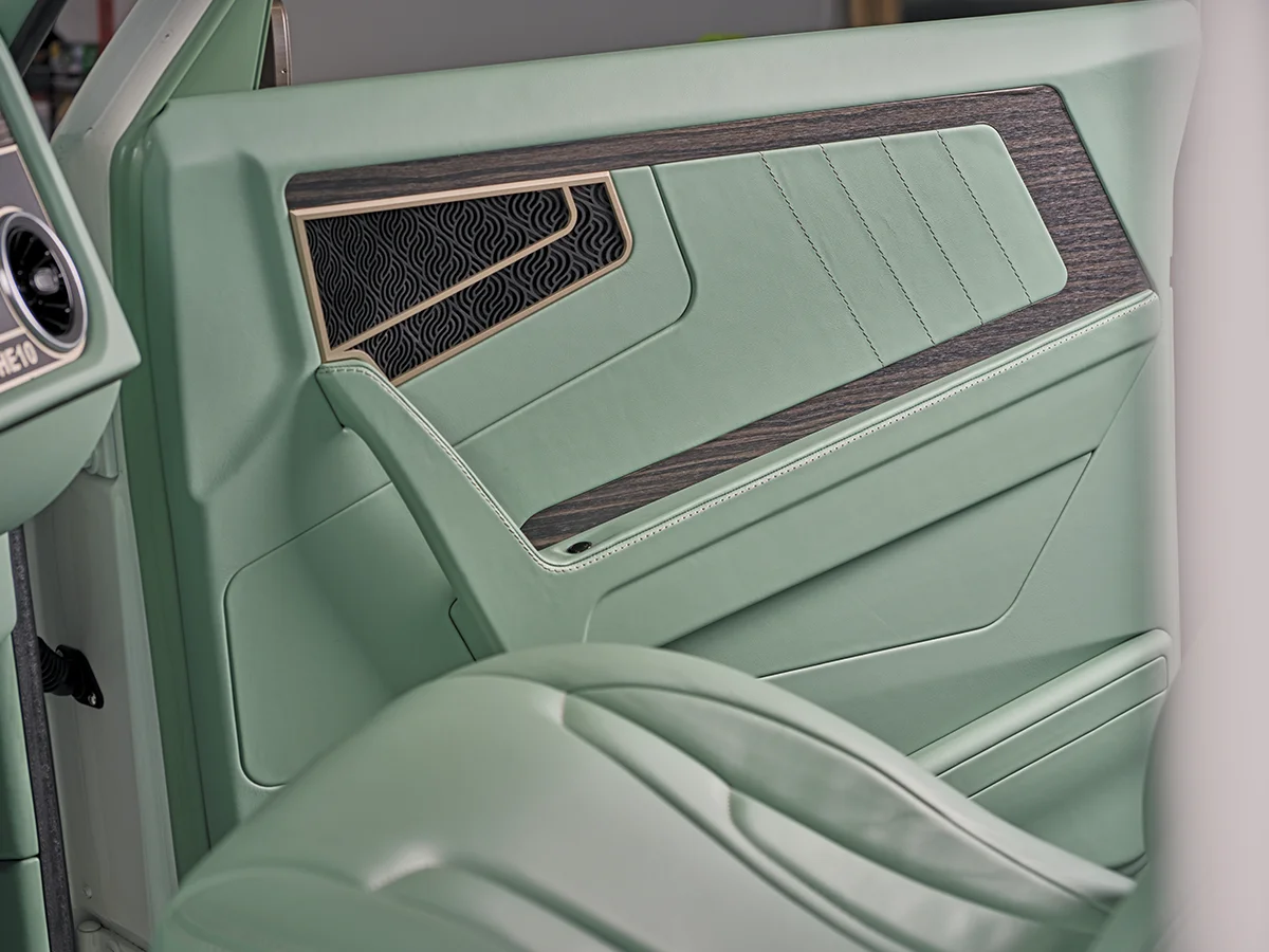 A close-up of a custom light mint-green truck interior, showing the door panel with wood grain trim and a dark, patterned inset, and the matching vinyl seat bolster in the foreground.