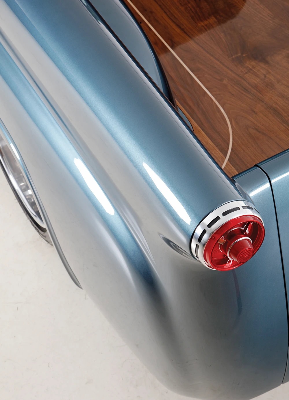 Close-up detail of a restored classic pickup truck's round red taillight, glossy blue fender, and finished wooden bed liner.