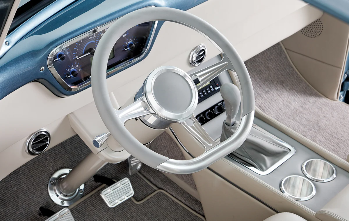 Interior cockpit of a custom vintage pickup truck featuring a modern gray steering wheel, custom instrument cluster, and center console with a shifter.