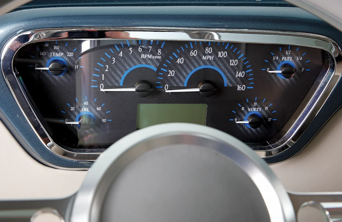 Close-up of a custom, modern digital instrument panel in a vintage pickup truck, featuring blue carbon fiber graphics and gauges for MPH and RPM.