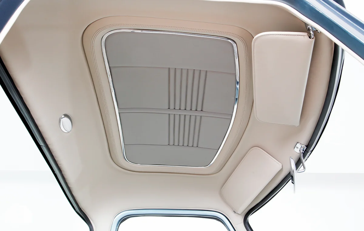 Custom interior headliner of a vintage pickup truck, featuring a cream-colored, stitched vinyl panel surrounded by chrome trim, and an integrated dome light.