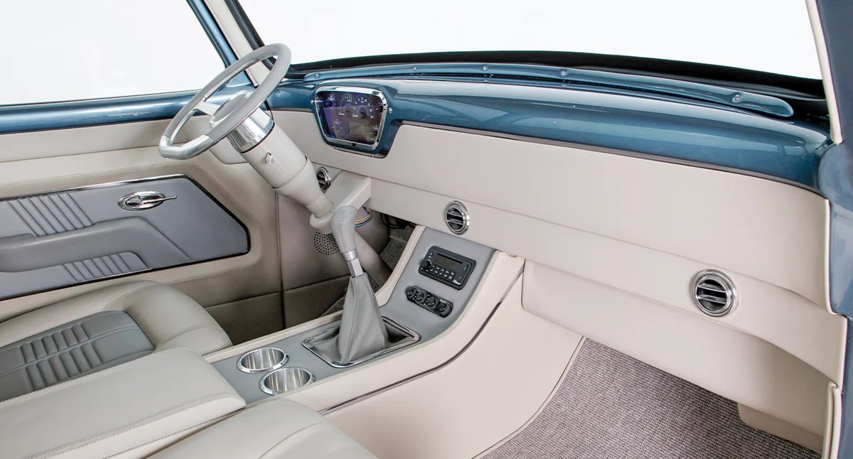 Wide view of a customized vintage truck interior, featuring a modern center console with cup holders, an automatic shifter, and a contemporary radio unit.