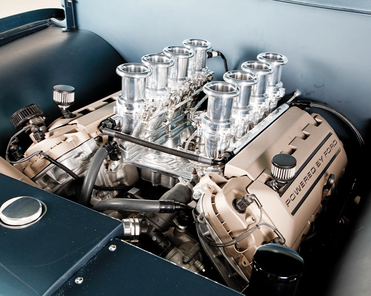 High-performance custom V8 engine with eight individual trumpet-style air intakes and a 'POWERED BY FORD' label on the valve covers.