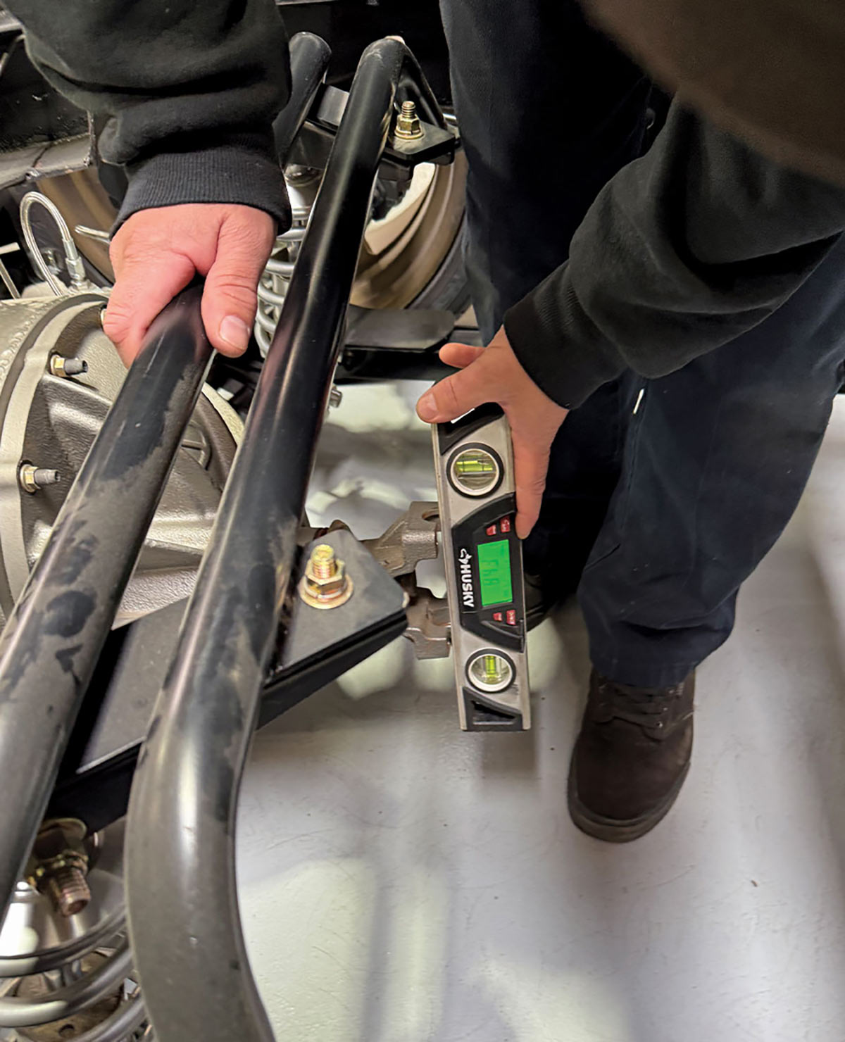 Technician using a Husky digital level to measure the angle and pinion of a custom four-link truck suspension or rear differential.